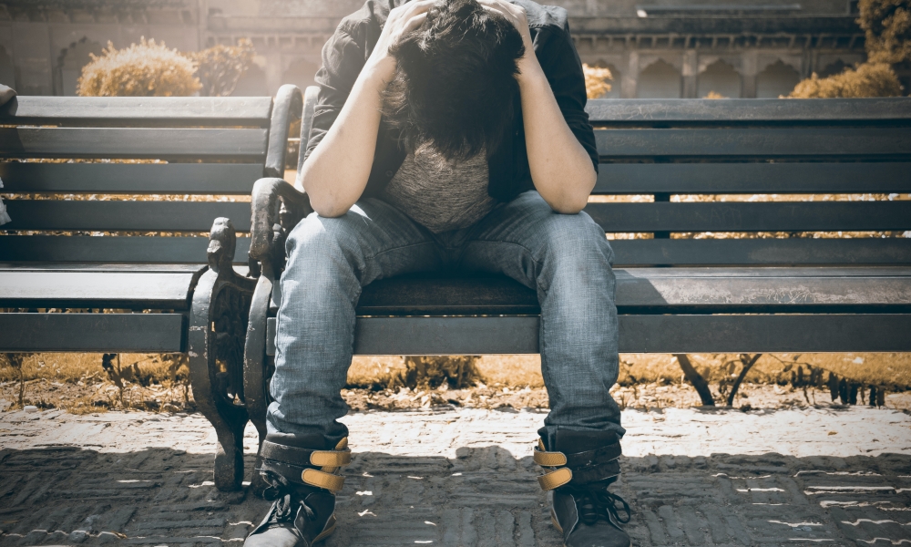 Man on bench with head in arms