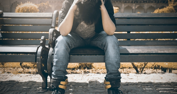 Man on bench with head in arms