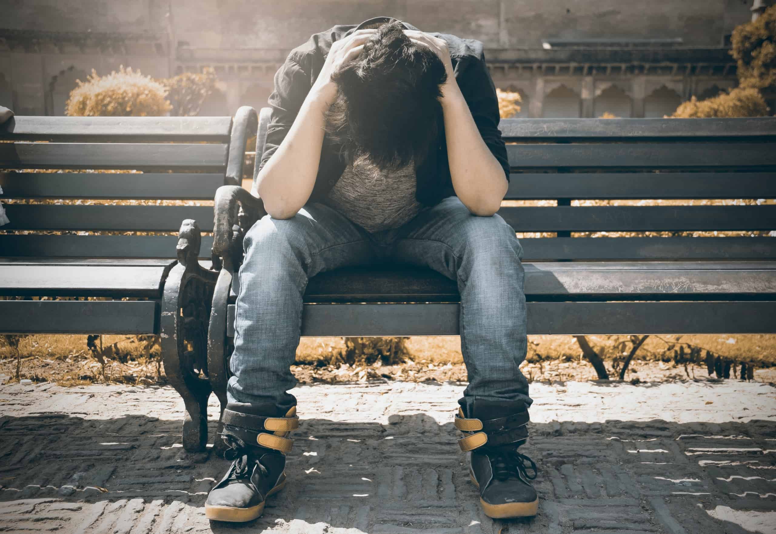 Man on bench with head in arms